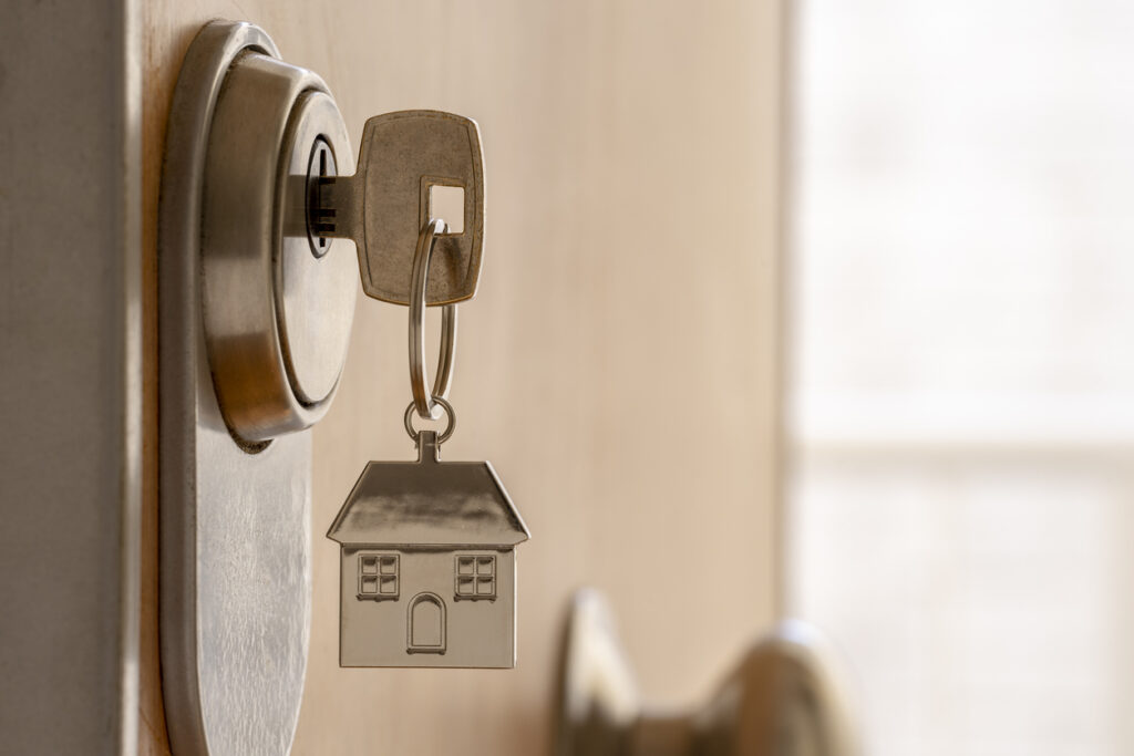 ISTOCK - CLOSE UP OF KEY AND HOUSE KEYCHAIN ​​IN HIGH SECURITY DOOR LOCK. HOME INSURANCE CONCEPT. COPY SPACE.